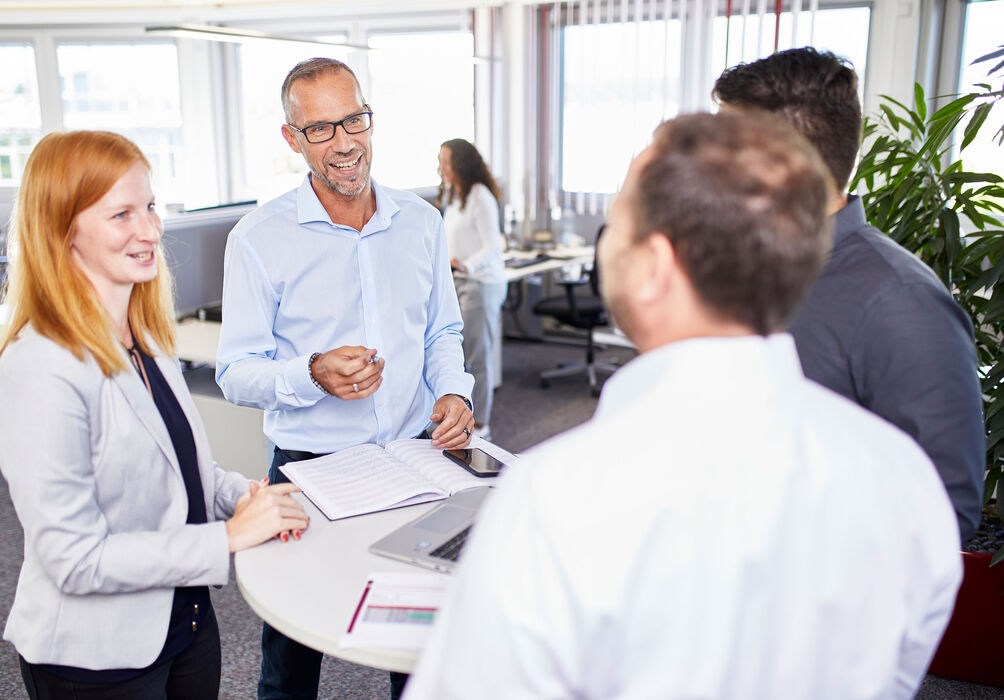 Gruppe steht um runden Tisch